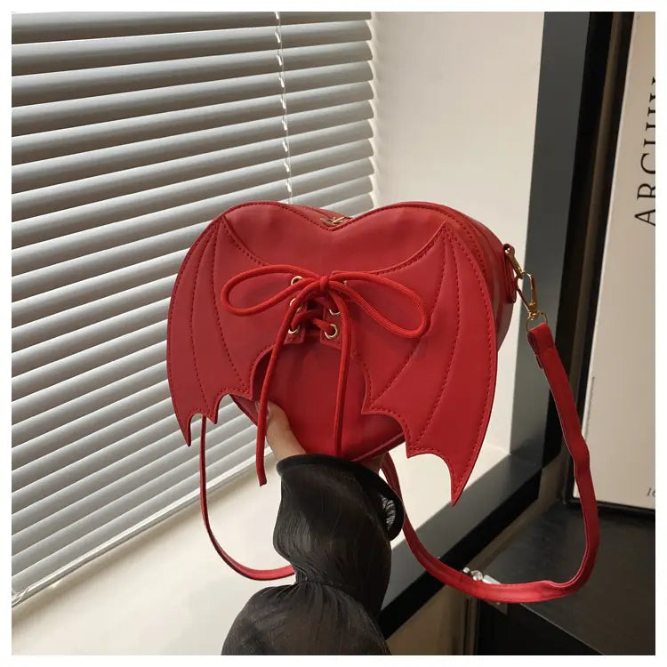 A vibrant red heart-shaped crossbody handbag with bat-wing details and a matching lace-up front.