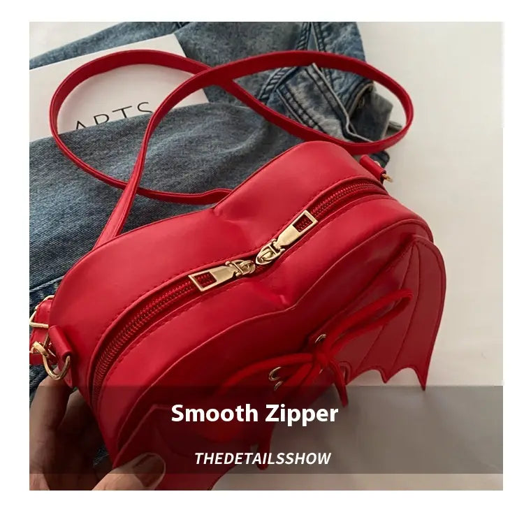 Vibrant red heart-shaped crossbody bag with gold-tone zipper and bat wing lace up detailing.