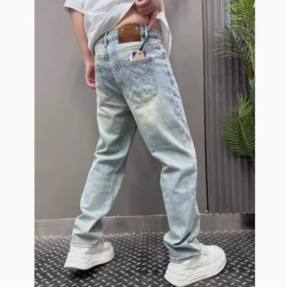 Men’s light wash relaxed straight leg denim jeans shown from the back with a faded, distressed look and a brown leather patch on the waistband.