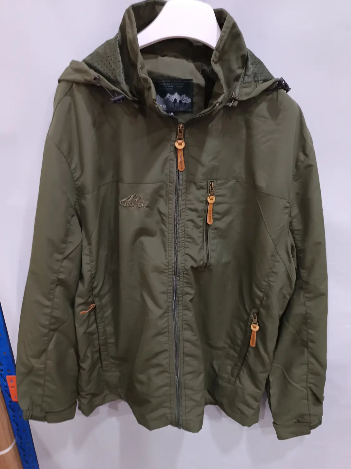 Chaqueta de senderismo con capucha impermeable color verde oliva, con tiradores de cremallera color camel y un logotipo de montaña en el pecho.