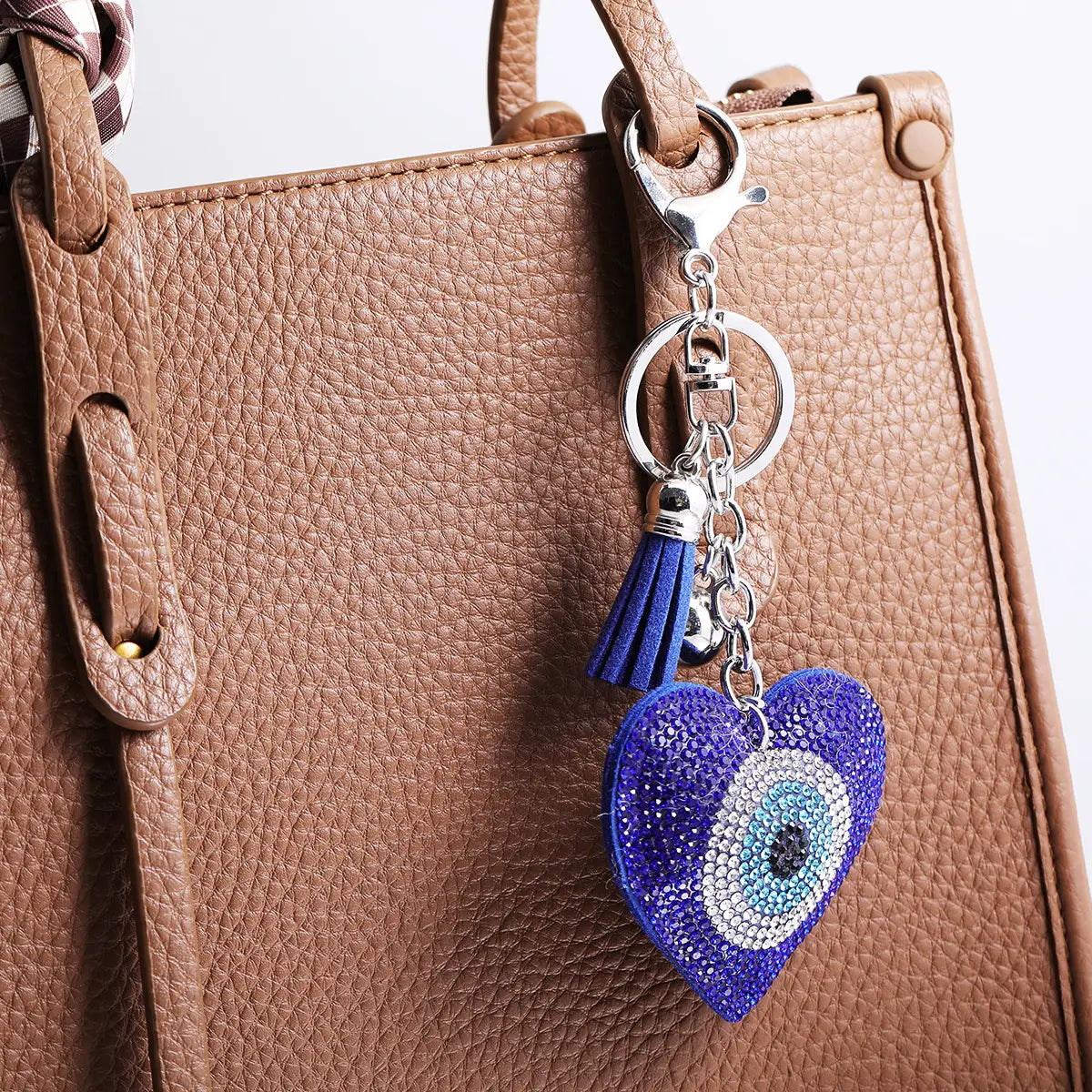 A sparkling blue heart-shaped evil eye keychain with rhinestones and a matching leather tassel attached to a silver-toned metal clasp.