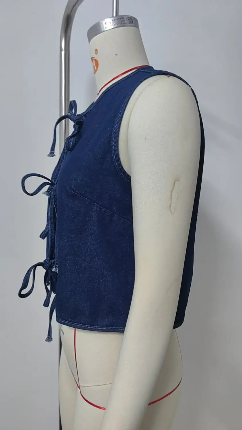 A navy blue denim sleeveless crop top with a front bow tie closure and side pockets designed in a Y2k style.