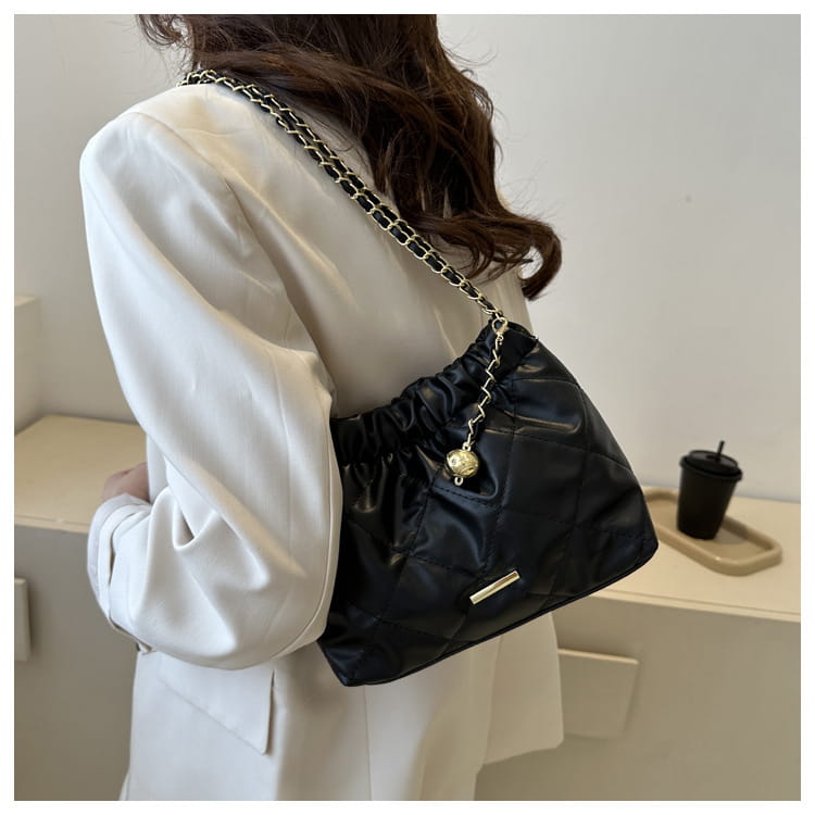 Black quilted faux leather crossbody bag with a silver chain strap and a gold-toned charm pendant.