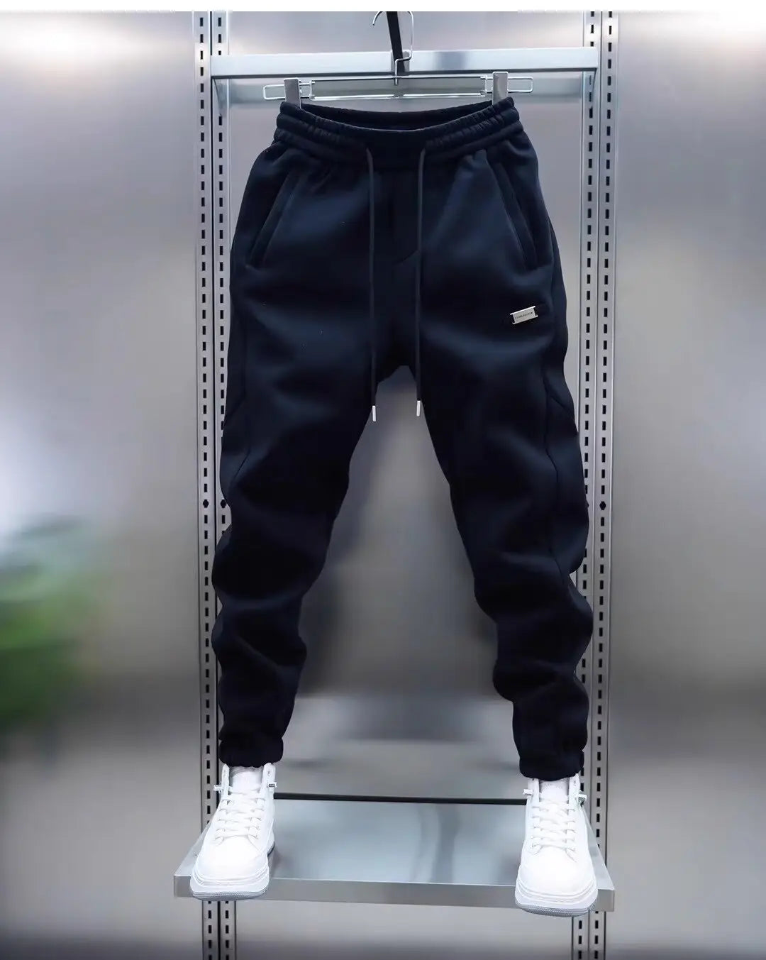 mens casual solid color sweatpants in black featuring a drawstring waistband subtle side pockets and a small metallic logo patch on the thigh