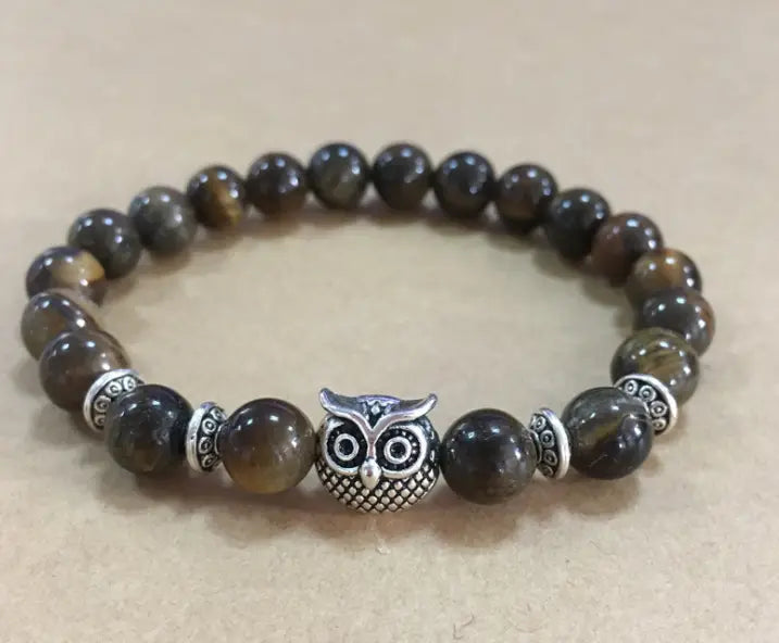 A natural lapis lazuli and lava stone owl charm bracelet features a silver owl charm and brown and gold tiger eye beads with metallic spacers.