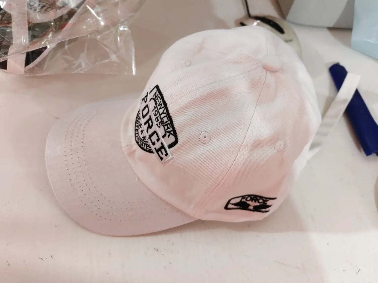 A white baseball cap made of fabric featuring a black embroidered new york police patch and a smaller logo on the side from the New York Force Embroidered Baseball Cap collection.