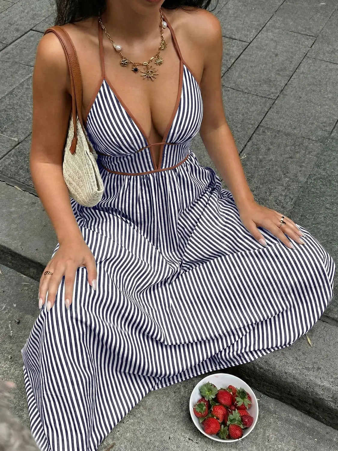 Une robe maxi à encolure type halter bleu marine et blanche à rayures verticales, avec une encolure en V plongeante, des lanières en cuir marron et une ceinture assortie, présentée de dos.