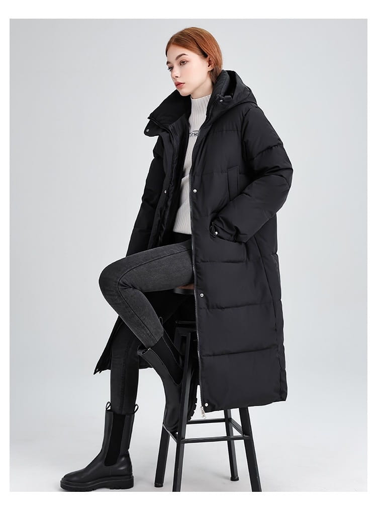 Manteau long matelassé à capuche pour femmes en noir, avec des panneaux matelassés, une fermeture éclair à l’avant et des fermetures boutonnées pour la chaleur et le style.