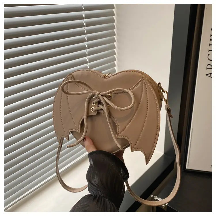 Beige bat wing heart crossbody bag with lace up detail and adjustable strap shown from the front.