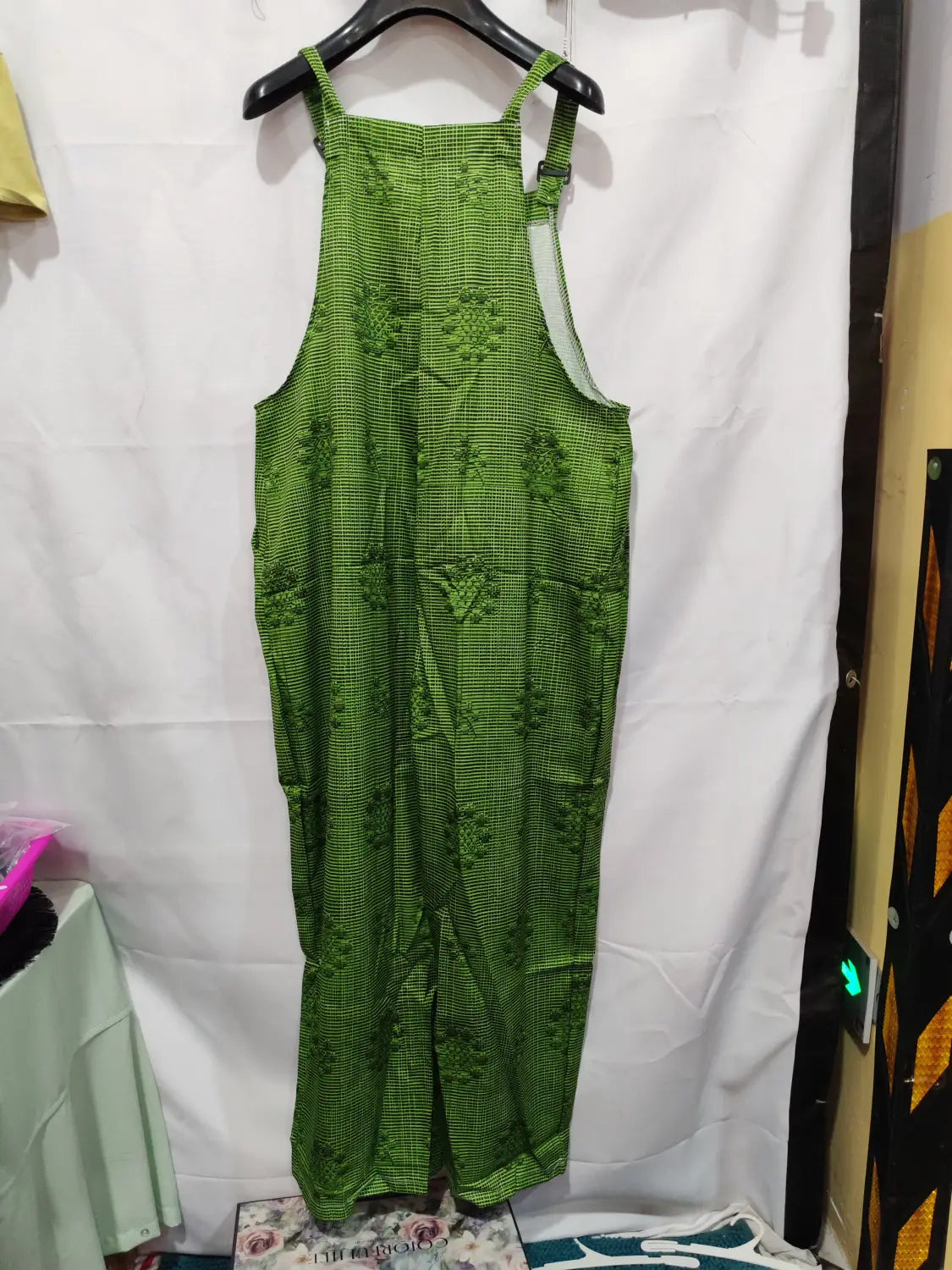 Green plaid suspender pants with 3d printed buttons and embroidered floral patterns hanging on a black hanger, designed as casual trousers.