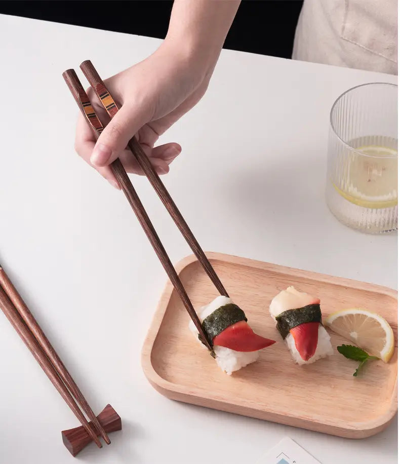 Dark brown wooden chopsticks with subtle metallic non slip tips held above sushi on a light wood tray in a wooden chopsticks set with non slip tips 10 pairs.