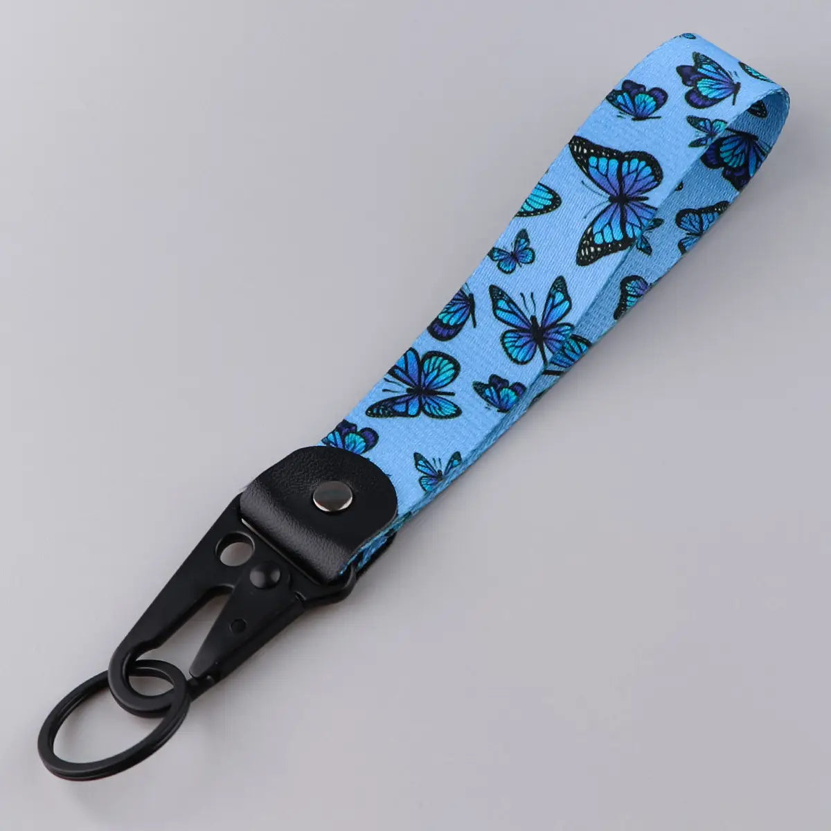 Light blue fabric butterfly wrist strap keychain with printed pattern and black metal carabiner clip for secure attachment.