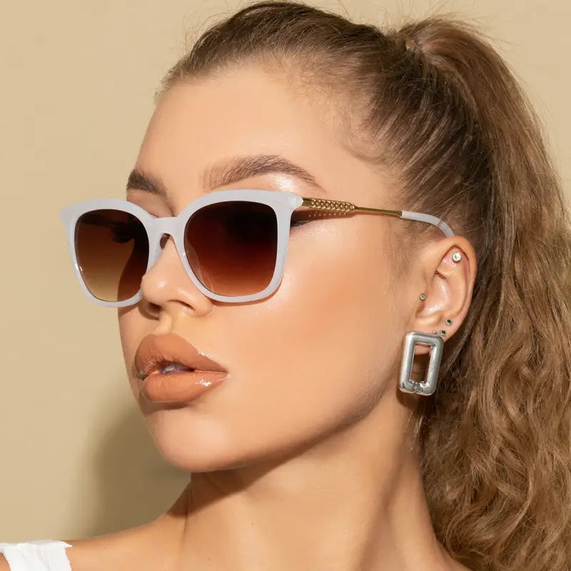 Vintage cat eye sunglasses featuring white frames with gradient brown lenses and gold tone temple details with chain embellishment.