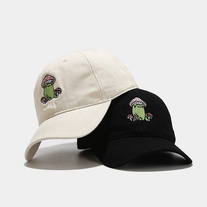Cream and black baseball caps featuring embroidered green frogs with pink-capped mushrooms titled frog mushroom embroidered baseball cap.
