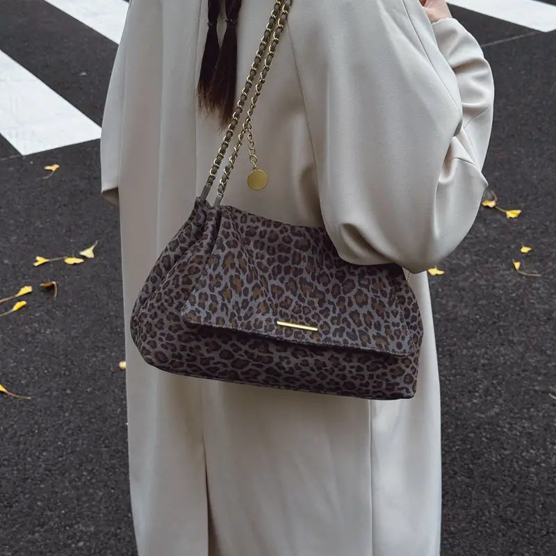 A taupe and black leopard print crossbody bag with a gold tone chain strap and clasp.