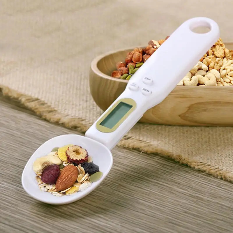 White digital spoon scale with small LCD screen and buttons filled with mixed nuts and dried fruits for precise kitchen measuring tool up to 500 grams
