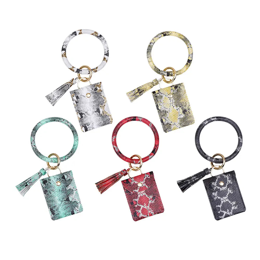 Porte-cartes avec mousqueton de poignet en cuir, avec gland, présentant une pochette rectangulaire à imprimé serpent dans des couleurs assorties.