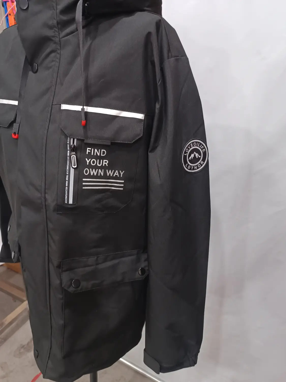 Men winter hooded parka coat in black with white reflective stripes, a front pocket featuring the text find your own way, and red zipper pulls.