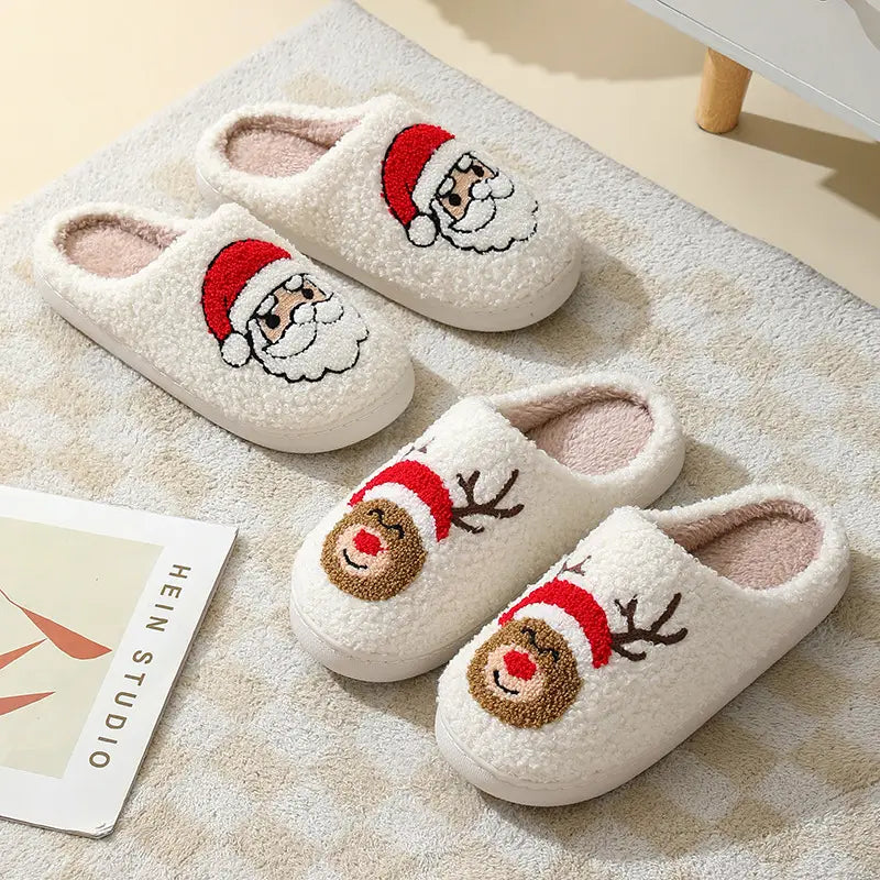 White plush festive embroidered santa and reindeer winter slippers featuring red hats brown antlers and pink lining.