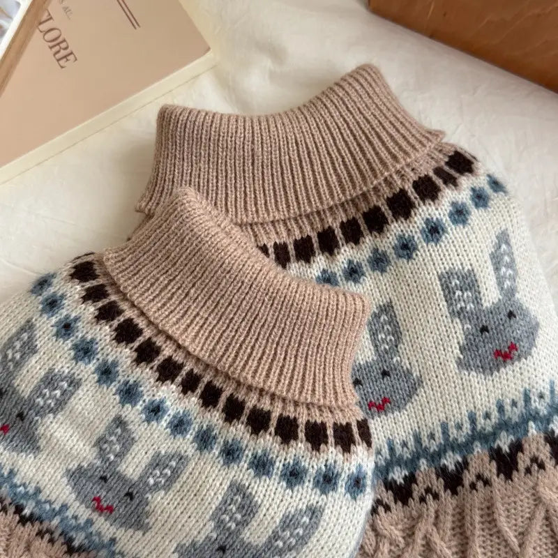Ein gemütlicher beiger Rollkragen-Hundepullover aus weichem Strick mit einem Fair-Isle-Muster, grauen Kaninchen und geometrischen Designs in Braun, Blau und Creme.