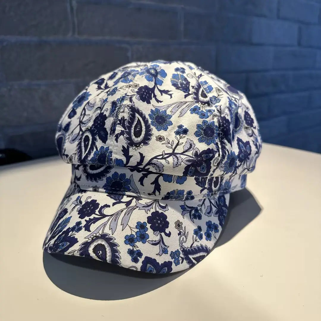A white fabric newsboy cap for women featuring a delicate blue and gray floral pattern with paisley motifs in black and white.