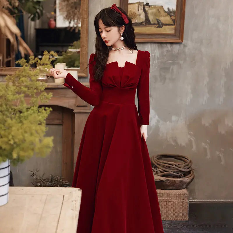 A burgundy velvet long sleeve a-line gown with a square neckline and a fitted bodice flaring into an elegant skirt.