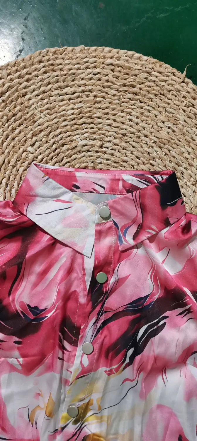 A women’s marble print satin long sleeve button blouse featuring a vibrant pink and black floral print with a crisp white collar and matching buttons.