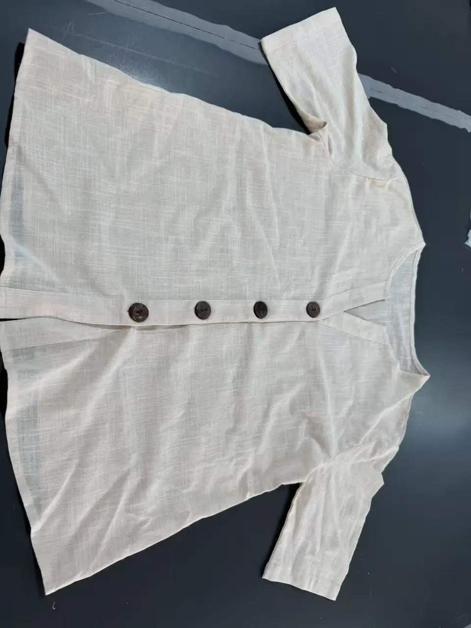 A cream-colored short sleeve button up cardigan for women made of textured linen-like fabric with dark brown buttons down the front.