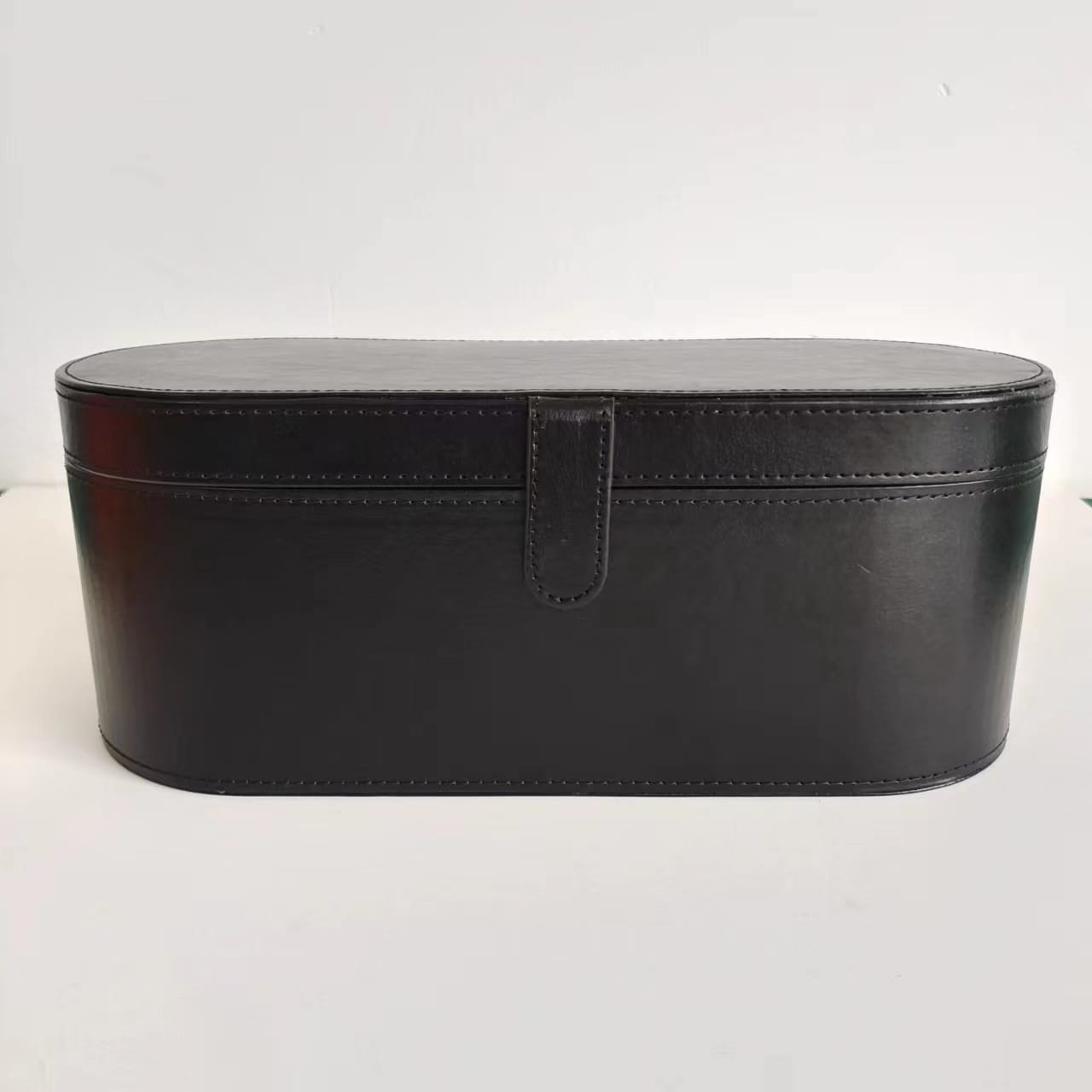 Black leather oval makeup case with flap closure and stitched detailing for 5-in-1 hot air comb hair dryer and styler set.