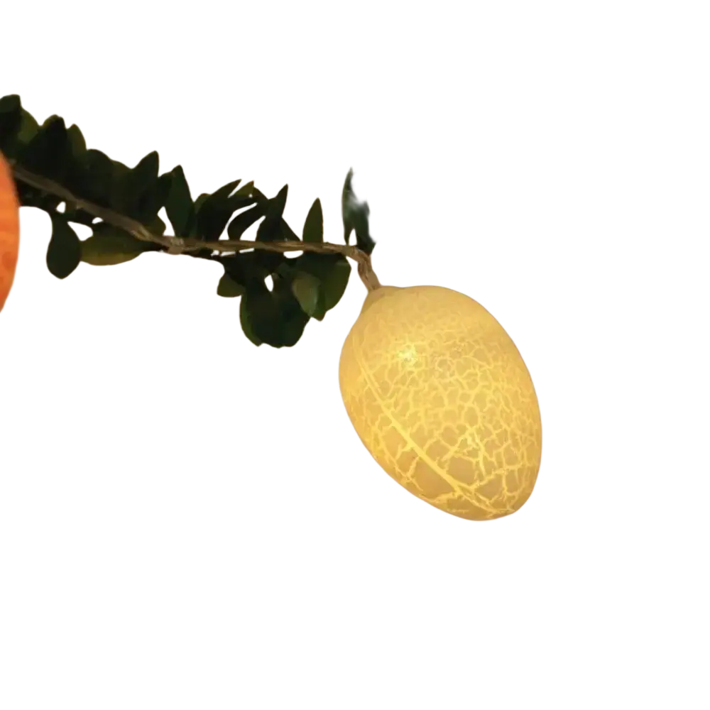 A glowing yellow egg-shaped led light with a crackled texture hanging on a green leafy garland for easter decor