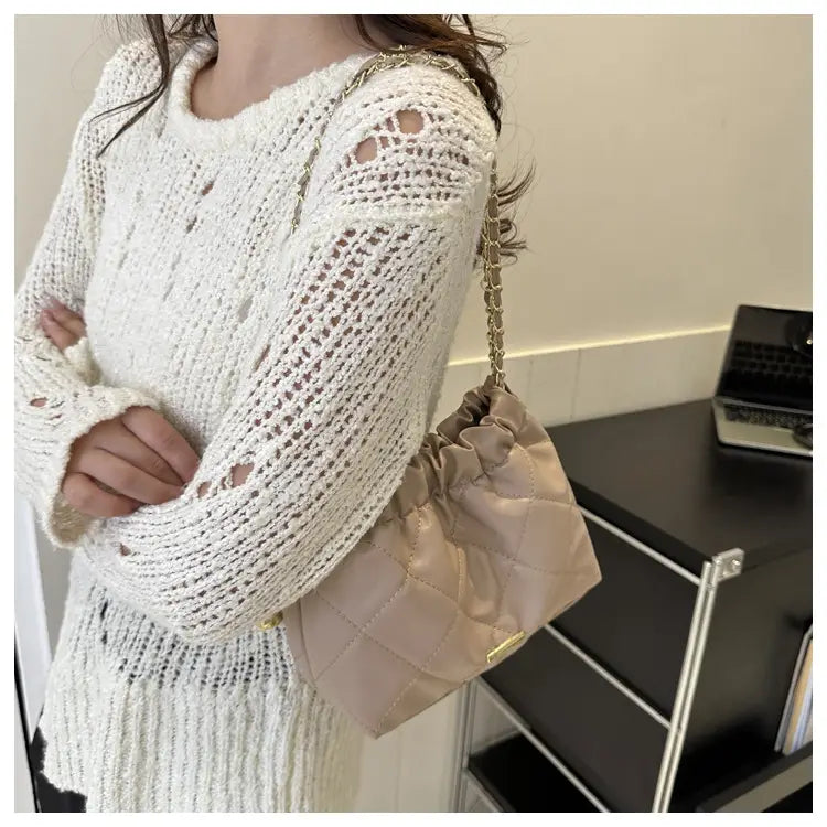 Beige quilted faux leather crossbody bag with drawstring closure and gold-tone chain strap.