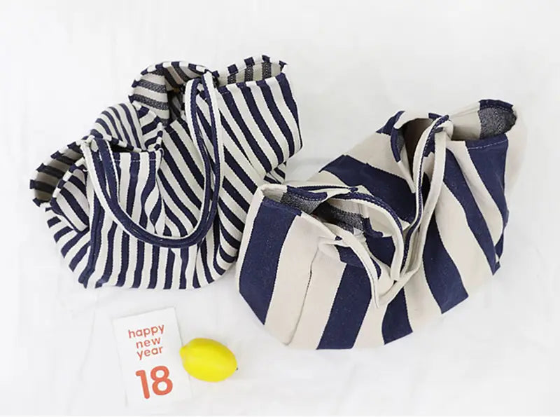 Two striped canvas tote bags in navy and white and cream and navy colors featuring high capacity and shoulder handles.