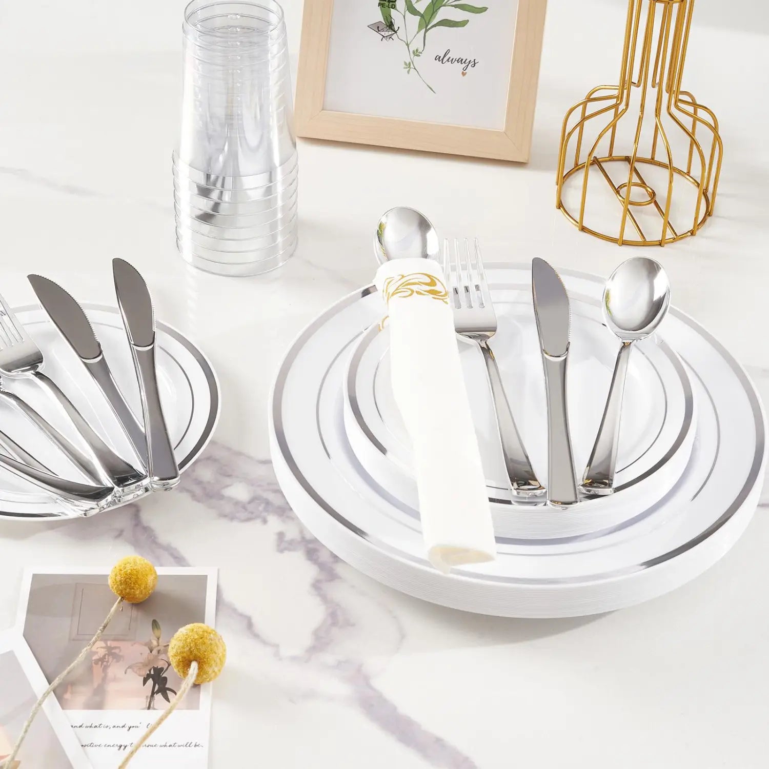 Set of silver-toned stainless steel cutlery neatly arranged on white plastic tableware plates with gold rim accents for 50 guests.