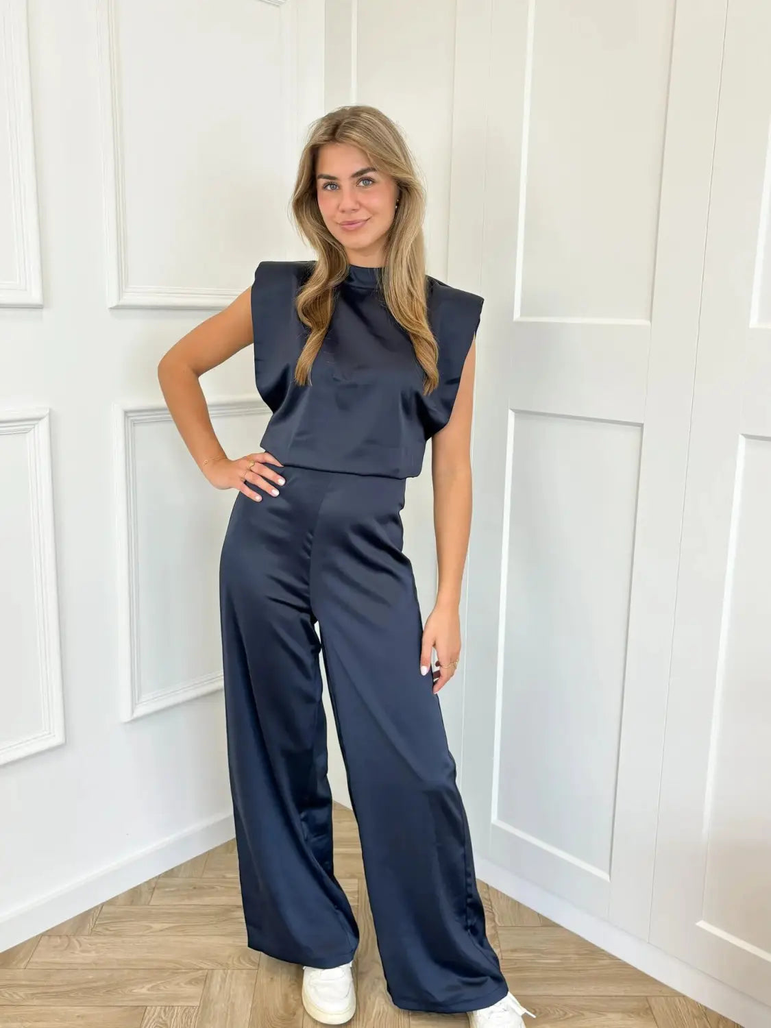 Navy satin backless evening dress jumpsuit with straight wide-leg pants and a sleeveless top featuring structured shoulder details shown from the back.