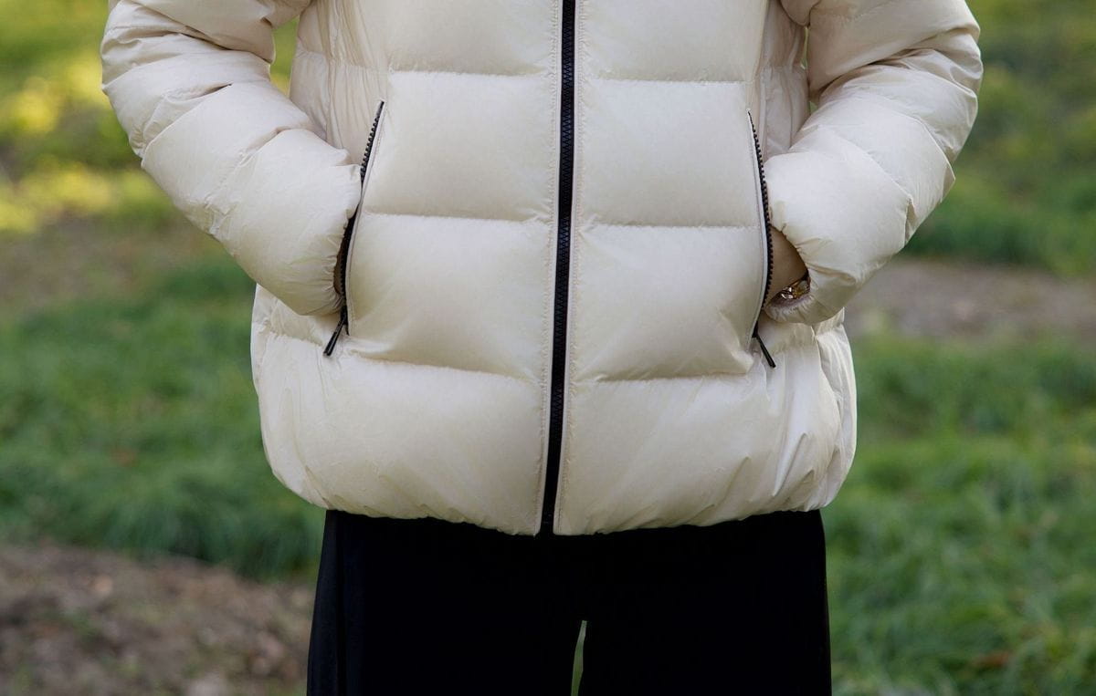 Cremefarbene kurze Steppjacke aus Daunen für Damen mit schwarzem Reißverschluss und Nahtdetails, ausgelegt für die Winterzeit.