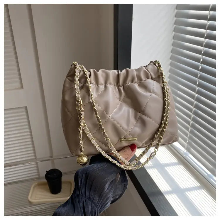 beige quilted faux leather crossbody bag with gold-tone chain strap and decorative bell charm.