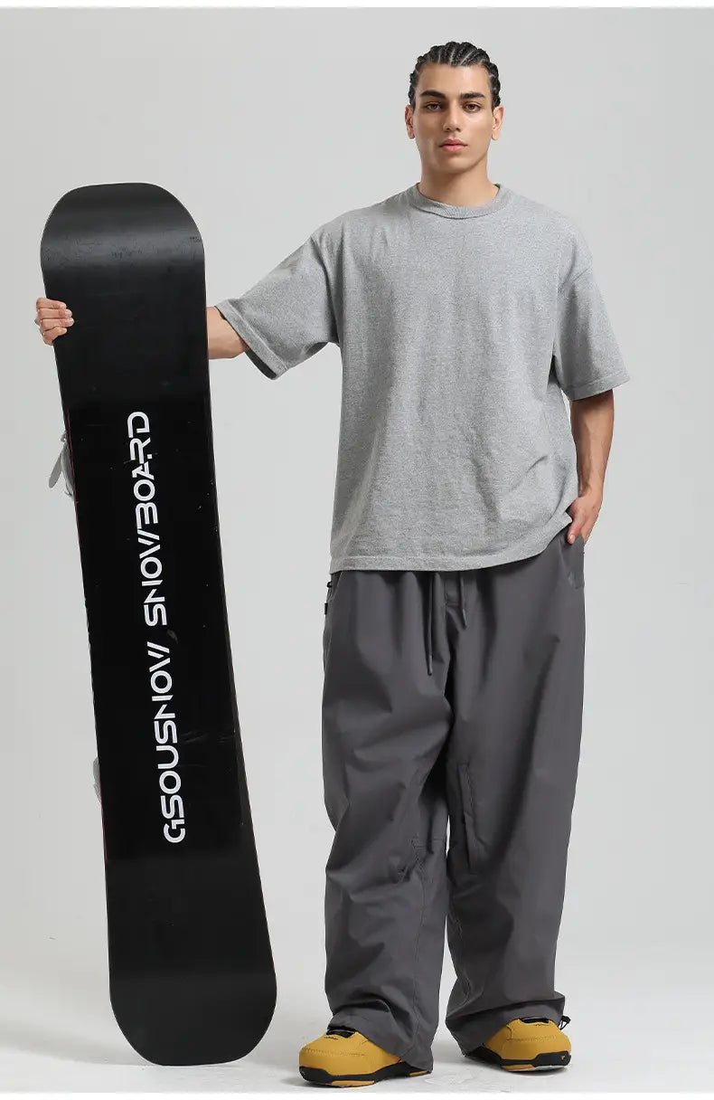 black snowboard with white vertical gsousnow snowboard lettering next to waterproof windproof loose work snow pants designed for outdoor use.