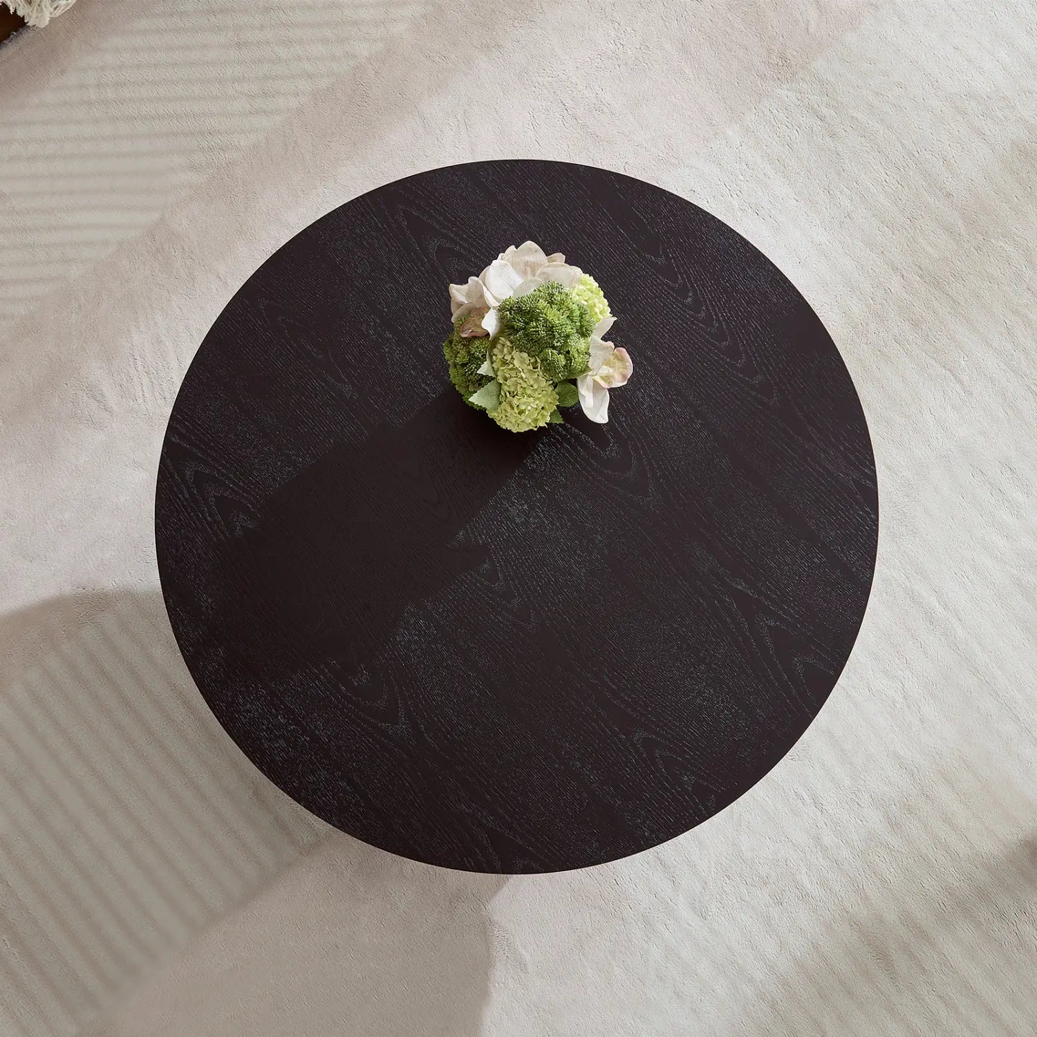 Mesa de centro redonda con acabado en madera oscura y un acento esculpido moderno que presenta una disposición floral central.