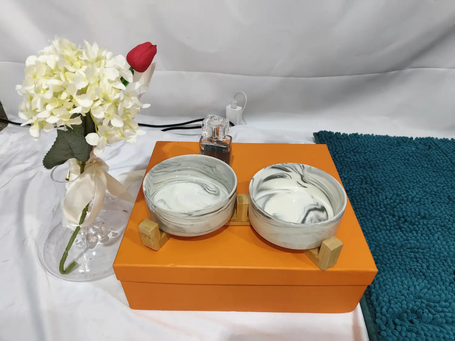 Ceramic double pet bowl with wood stand featuring two white and gray marbled ceramic bowls presented on an orange box.