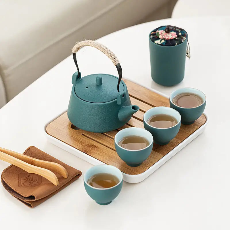 teal cast iron tea kettle with woven rope handle and black metal accents featured in a ceramic travel tea set with bamboo tray and case