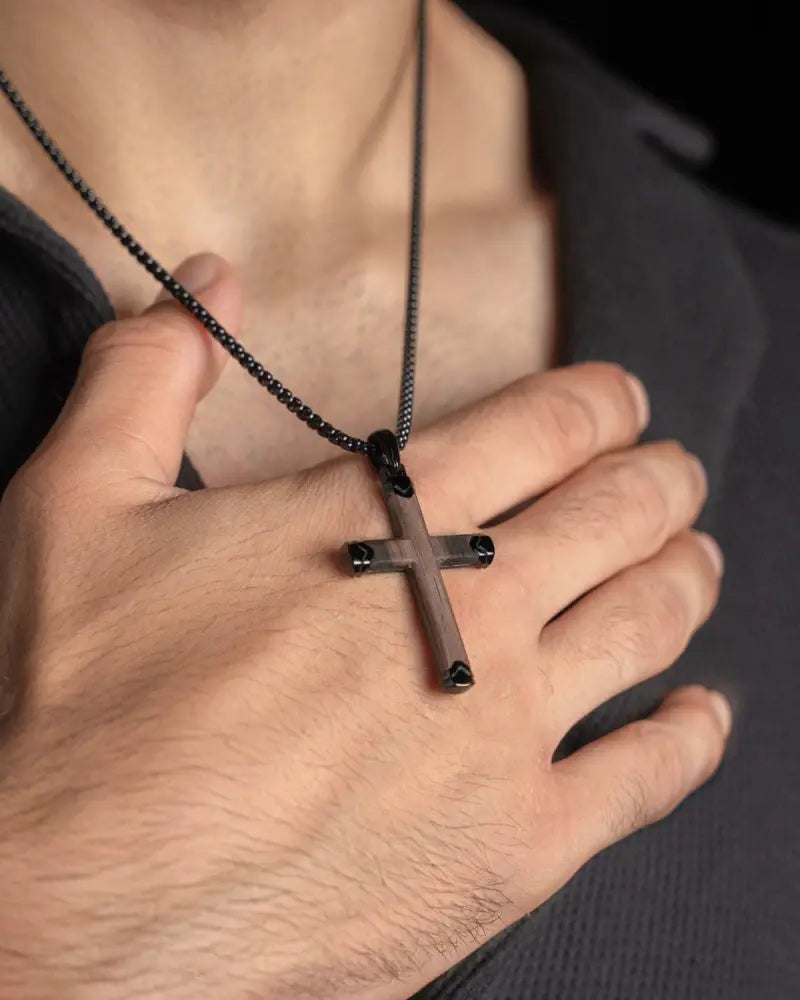A sleek black stainless steel cross necklace with matte ebony wood finish and spherical accents on a beaded chain