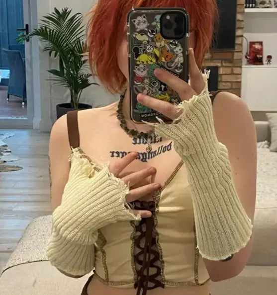 A cream-colored ribbed knit fingerless glove with frayed edges and brown leather straps, shown from the back side, designed as a black tattered knit fingerless glove unisex.