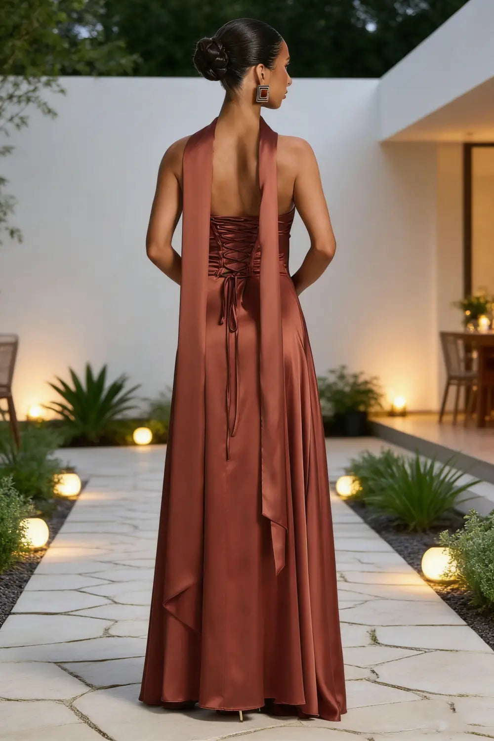 Un vestido de noche de satén en color óxido, fluido y sin tirantes, con escote tipo halter y cordones del corsé en la espalda, que muestra el lado posterior del elegante vestido sin tirantes de satén con escote drapeado