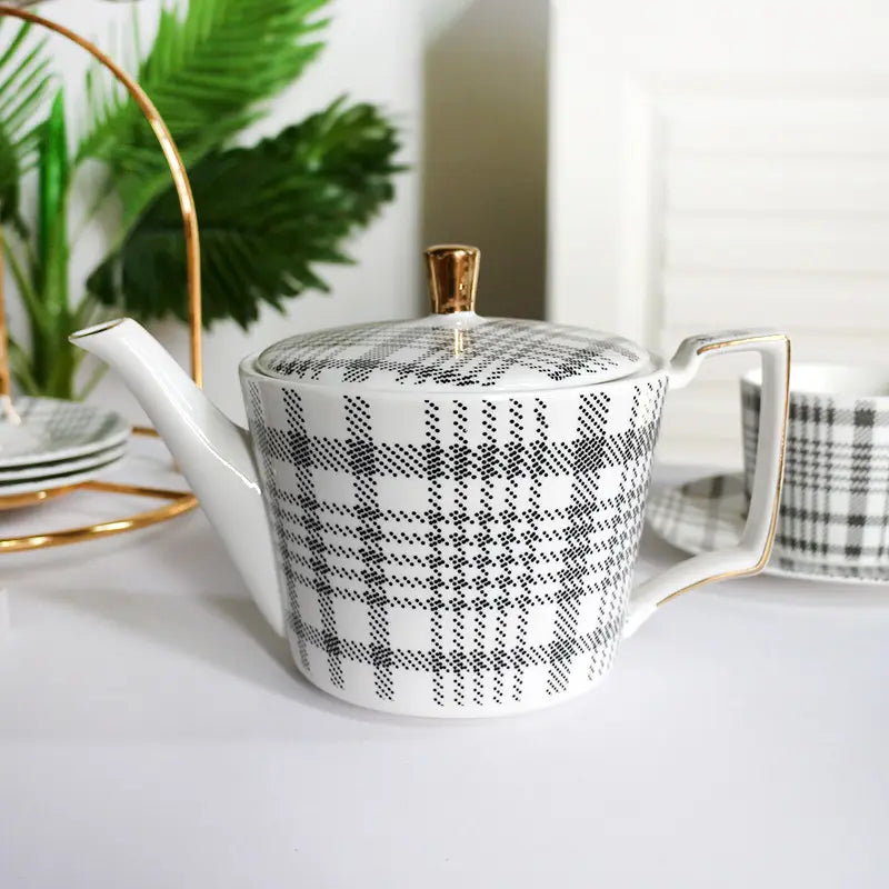 White ceramic teapot with a black plaid pattern and gold-trimmed lid handle and spout in a ceramic tea set with plaid teapot and gold trim tray.