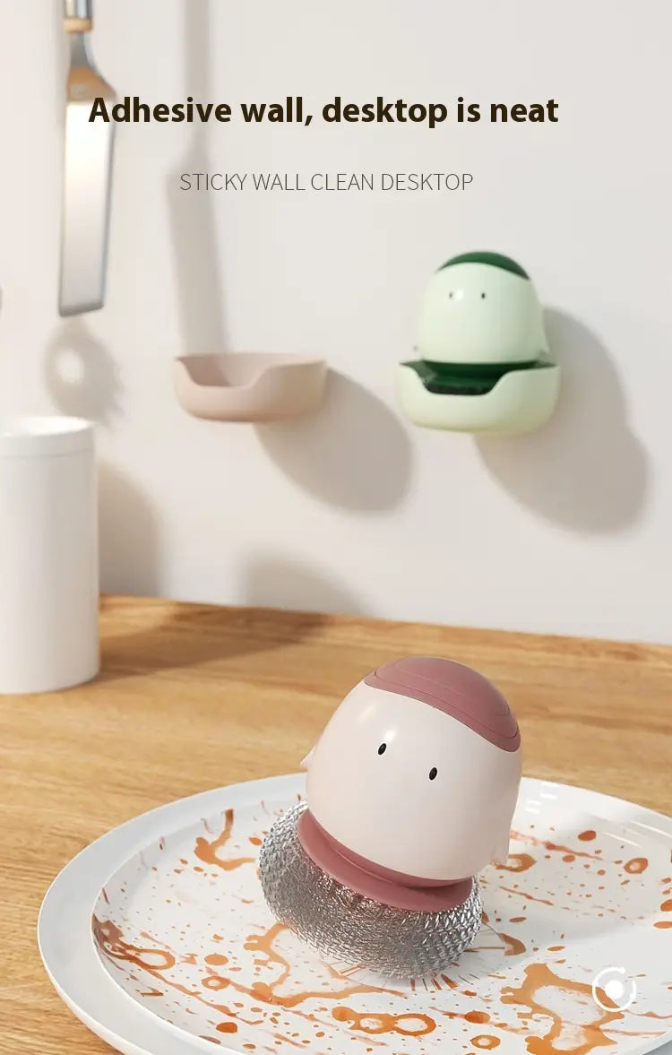 un récurant-distributeur automatique de savon liquide en forme d’œuf, mignon, avec un haut rose et un corps blanc, posé sur un récurant en maille argentée dans une assiette.