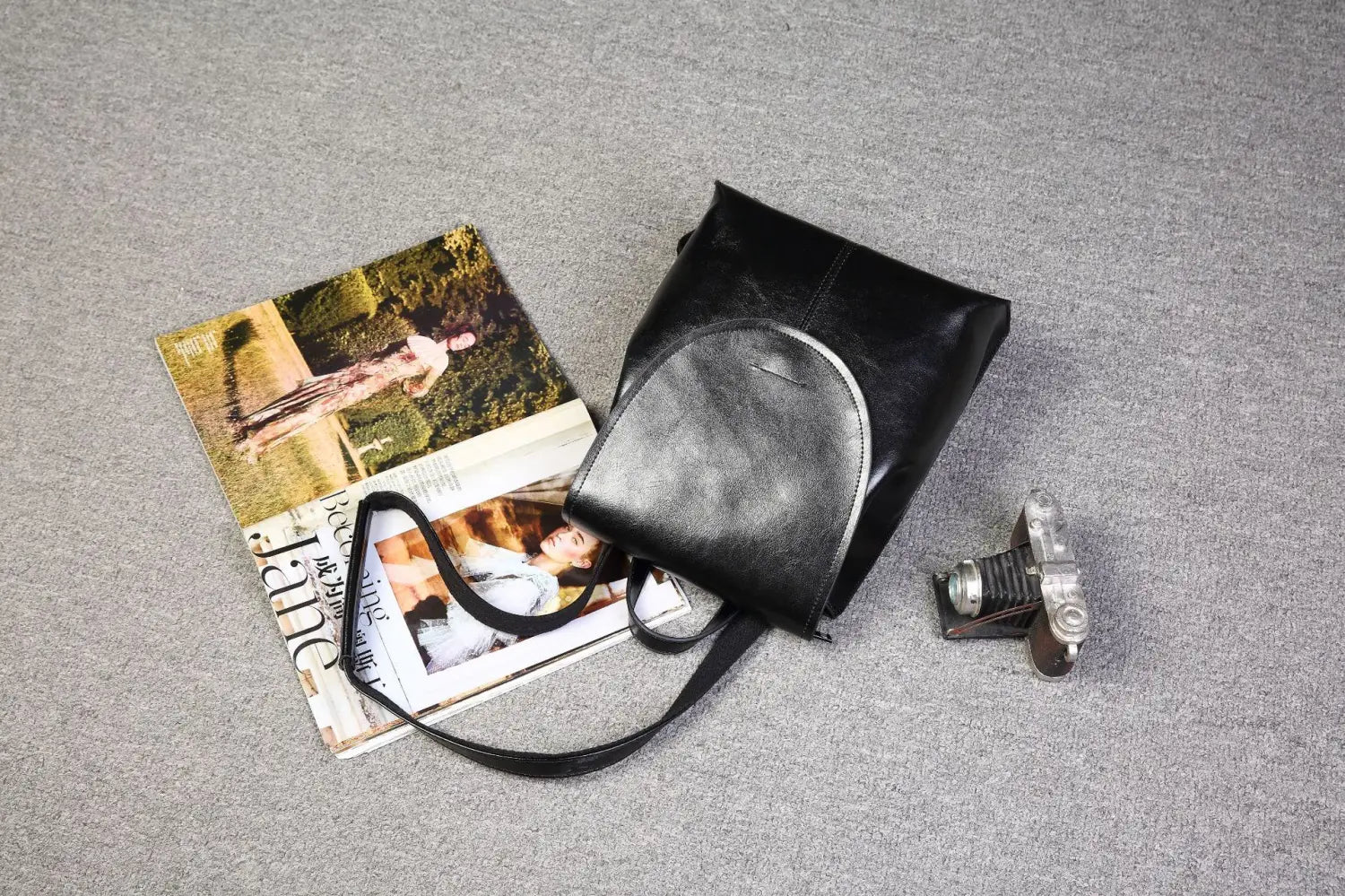 Mochila bandolera de cuero negro con parte superior curva y correa de hombro ajustable, en estilo de moda retro.