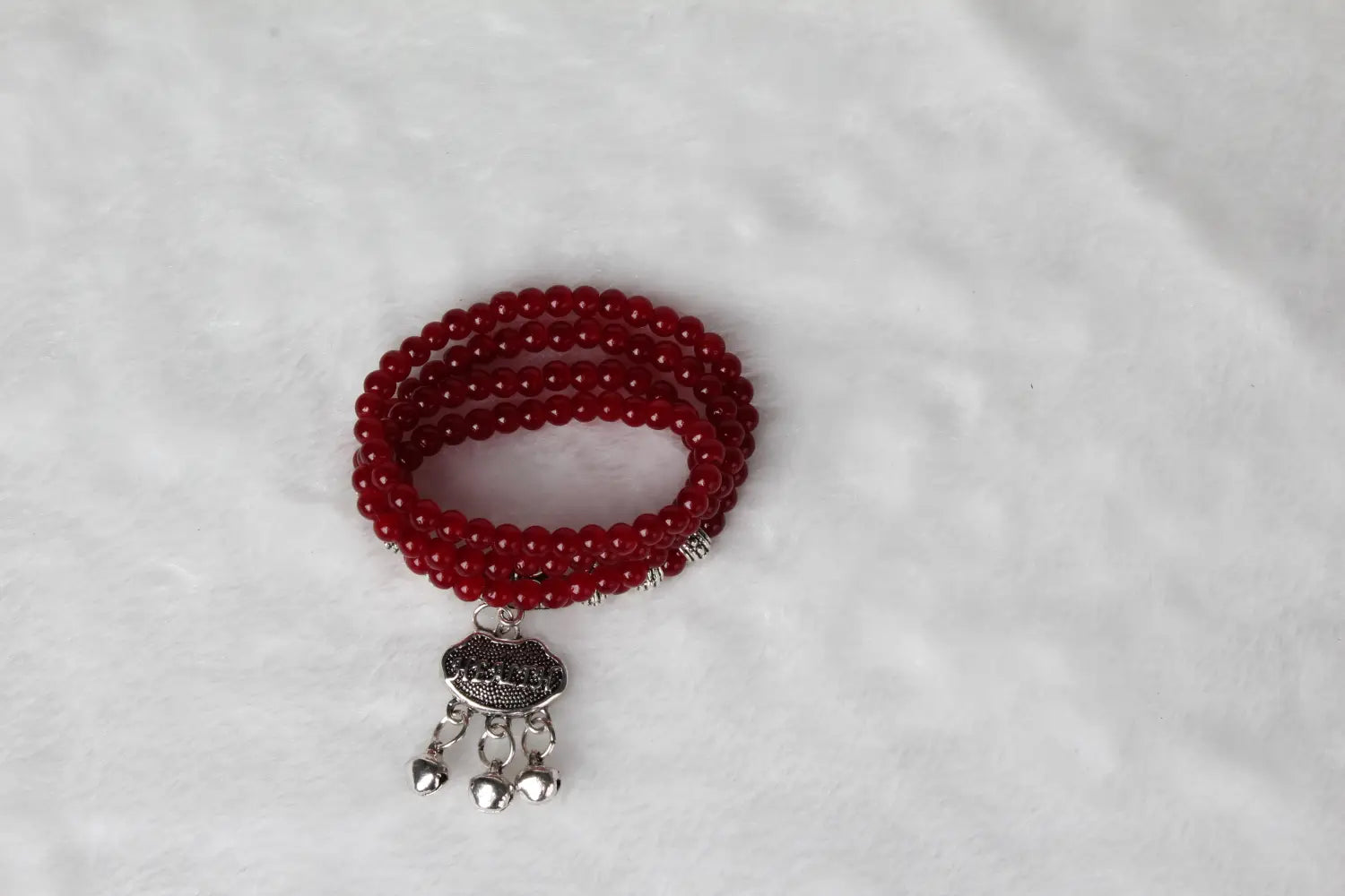 Red agate good luck bracelet featuring red beads with a silver-toned engraved protect charm pendant and dangling bells.