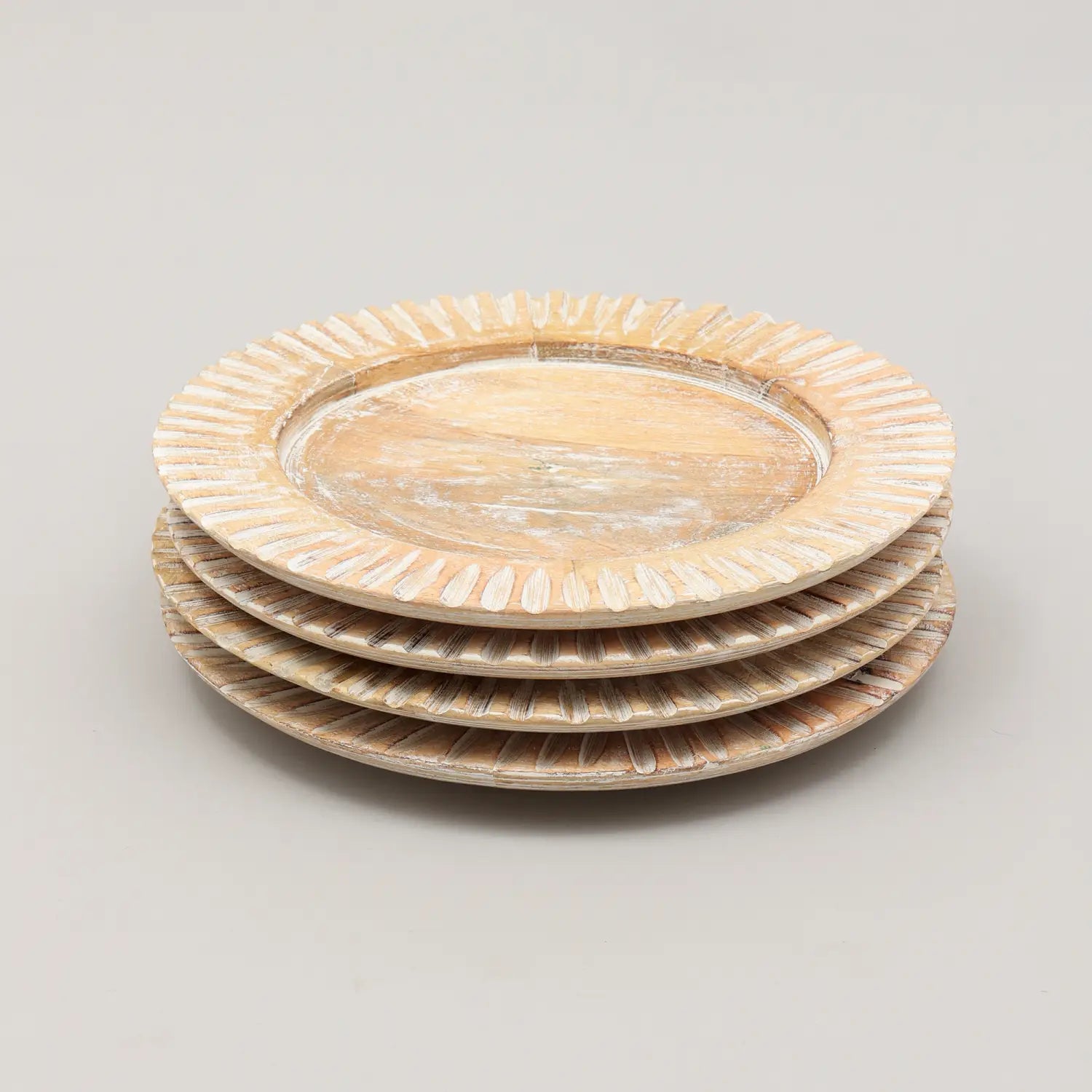 Lot empilé de quatre sous-assiettes en bois artisanal blanc pour assiette de 13 pouces, avec une finition patinée et un design à bord festonné.