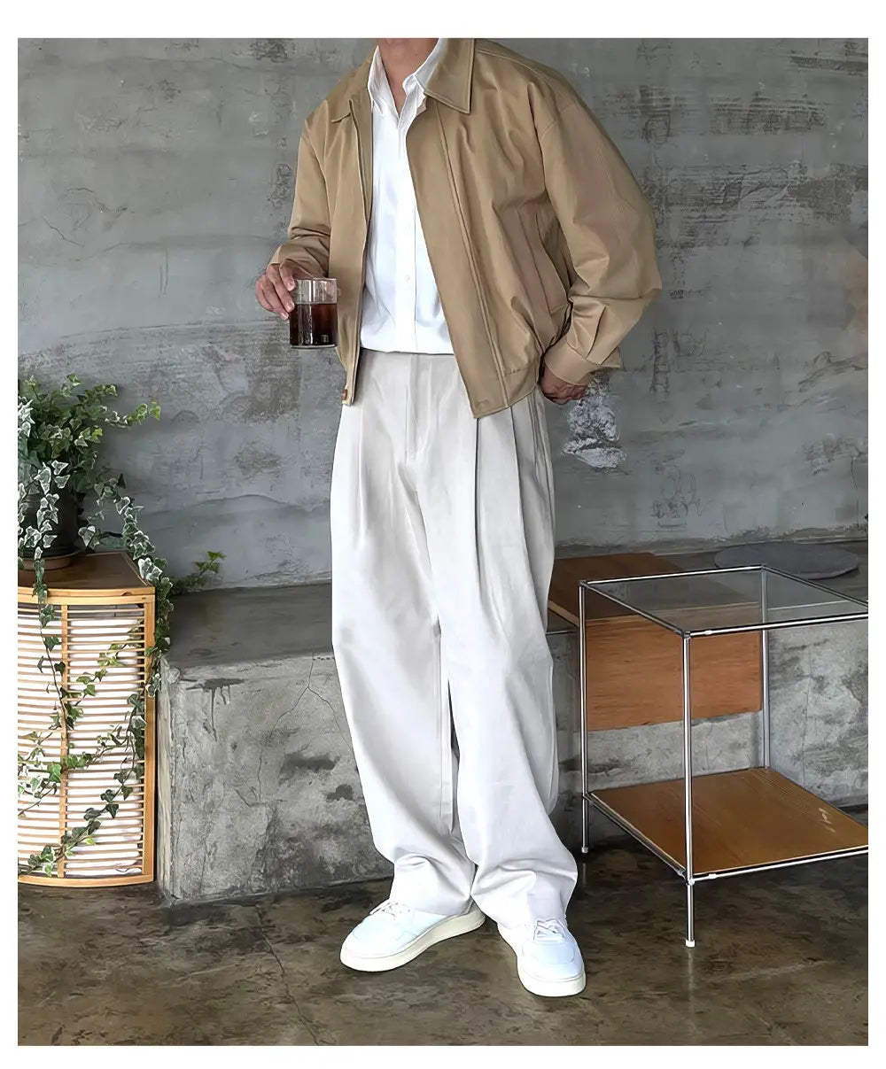 Chaqueta bomber beige con cuello clásico y detalles de costura sutiles, combinada con pantalones de vestir anchos plisados color gris oscuro para hombre