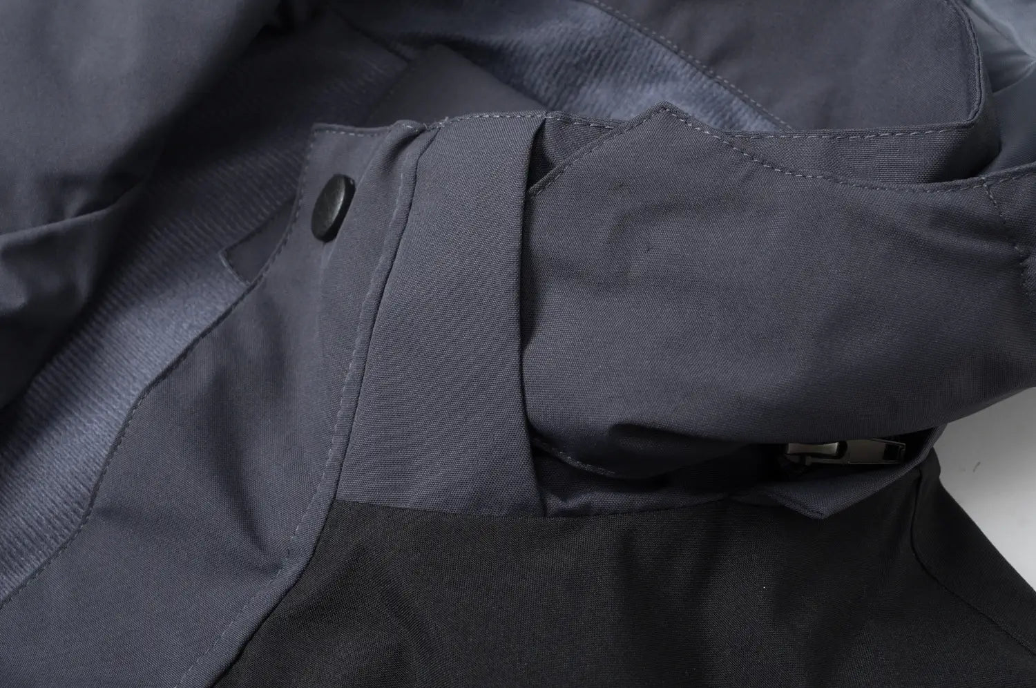 Veste de plein air imperméable à capuche en nylon gris foncé pour hommes et femmes, avec des détails de boutons et de fermeture éclair noirs.